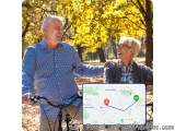 The image shows an elderly couple on a bicycle in a park. The man is on the left side of the image, wearing a blue checkered...