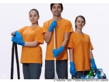 The image shows three people, two women and a man, wearing orange t-shirts and blue gloves. They are standing in front of a w...