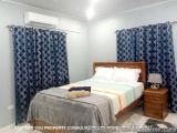 The image shows a bedroom with a single bed in the center. The bed has a wooden headboard and is covered with a gray and whit...