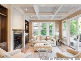 The image shows a spacious living room with a high ceiling and white walls. The room has a large window on the right side, al...