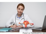 The image shows a young woman doctor sitting at her desk with a laptop and a model of a human reproductive system in front of...