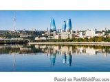 The image is a panoramic view of a city with a body of water in the foreground. The water is calm and reflects the buildings...