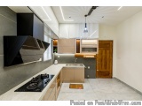 The image shows a modern kitchen with a minimalist design. The kitchen has a large island with a black stove and a black rang...