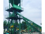 The image shows a large green industrial structure with a sign that reads "DESIGN" on the top. The structure appears to be a...