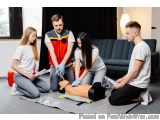 The image shows a group of four young people, two men and two women, kneeling on the floor in a living room with a dummy on a...