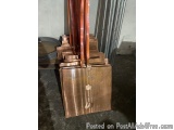The image shows a stack of copper-colored metal objects in a warehouse or workshop. The objects appear to be made of metal an...