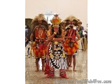 The image shows three people dressed in traditional Balinese costumes. The person in the center is wearing a black and white...
