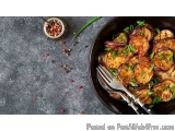 The image shows a black bowl filled with a dish of eggplant and red onion. The eggplant is cooked to a golden brown color and...