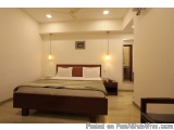 The image shows a modern and minimalist bedroom with a large wooden bed in the center. The bed has a wooden headboard and foo...