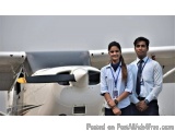 The image shows a young couple standing in front of an airplane. The airplane is white with a propeller and a blue stripe on...