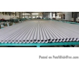 The image shows a large warehouse with a long table in the center. On the table, there are multiple rows of white pipes arran...