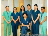 The image shows a group of nine women in blue scrubs standing in a hospital corridor. They are all smiling and posing for the...