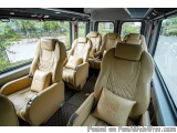 The image shows the interior of a luxury bus. The seats are upholstered in a light beige leather with a quilted pattern. Each...