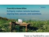 The image shows a wooden desk with a laptop and a chair on it, set up on a grassy hill overlooking the ocean. The sky is blue...