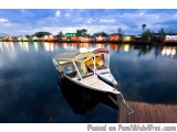 The image shows a small boat docked at a pier on a lake. The boat is white with a red and yellow canopy and has a white rope...