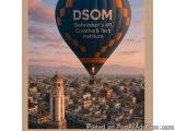 The image shows a hot air balloon flying over a city. The balloon is blue and orange in color with the words "DSOM Dehradun's...
