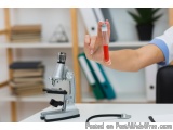 The image shows a person's hand holding a small test tube with a red liquid in it. The test tube is being held up by a person...