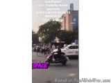 The image shows a busy street scene in Janakpur, India. There are several vehicles on the road, including a red scooter and a...