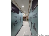 The image shows a long corridor in a medical gym. The corridor has a white tiled floor and a blue wall on the left side. On t...
