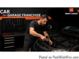 The image shows a man working on a car in a garage. He is wearing a black t-shirt and overalls and is holding a wrench in his...