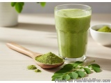 The image shows a glass of green smoothie on a wooden table. The smoothie is made from moringa leaves and is a vibrant green...