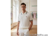 The image shows a young man standing in a clothing store. He is wearing a white polo shirt with a blue and yellow striped col...