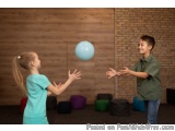 The image shows two young children, a boy and a girl, playing with a blue balloon in a room with a brick wall in the backgrou...