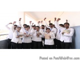 The image shows a group of young people, likely students, standing in a room with their arms raised in the air. They are all...