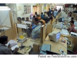 The image shows a busy office space with multiple desks and computers. There are several people sitting at the desks, some of...