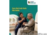 The image shows an elderly man in a wheelchair with a nurse sitting next to him. The nurse is wearing a blue uniform and is h...