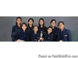 The image shows a group of nine young girls in school uniforms, all of them smiling and posing for a photo. They are standing...