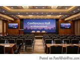 The image shows a conference hall in Ahmedabad, India. The hall has a large screen in the center of the room with the words "...