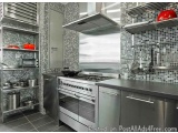The image shows a modern kitchen with a stainless steel color scheme. The kitchen has a large island with a gas stove and a r...