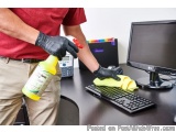 The image shows a person wearing a red t-shirt and black gloves, cleaning a computer desk with a yellow microfiber cloth. The...