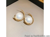 The image shows a pair of gold earrings with a white pearl in the center. The earrings are circular in shape and have a thin...
