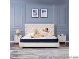 The image shows a modern bedroom with a large white bed in the center. The bed has a tufted headboard and a blue mattress wit...