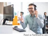 The image shows a man wearing a headset and smiling while sitting at a desk in front of a computer. He appears to be in a cal...