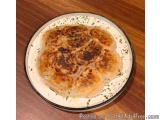 The image shows a round plate with a white rim and a black rim. On the plate, there is a dish that appears to be a type of br...
