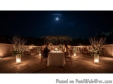 The image shows a romantic dinner on a rooftop at night. The sky is dark and the moon is visible in the top right corner. The...