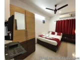 The image shows a modern and spacious bedroom with a large bed in the center. The bed has a white comforter and red pillows,...