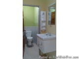 The image shows a small bathroom with a white sink and a white toilet. The walls are painted in a light green color and the f...