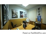 The image shows an office space with a desk and a computer monitor on it. The desk is in the center of the room and has a bla...