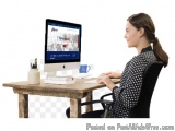 The image shows a young woman sitting at a wooden desk in front of a computer monitor. She is wearing a black and white polka...