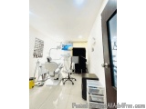 The image shows a dental clinic room with a white tiled floor and white walls. On the left side of the room, there is a white...