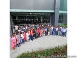 The image shows a group of people standing in front of a modern building with a glass facade. The building appears to be a un...