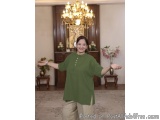 The image shows a woman standing in a room with a chandelier hanging from the ceiling. She is wearing a green blouse and beig...