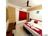 The image shows a hotel room with a large double bed in the center. The bed is covered with white linens and red pillows, and...
