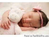 The image is a close-up of a newborn baby sleeping peacefully on a white blanket. The baby is wearing a pink headband with a...
