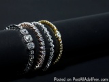 The image shows a stack of three bracelets on a black background. The bracelets are made up of different colors - black, silv...