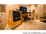 The image shows a modern home recording studio setup. The room has a wooden desk with a large wooden cabinet on the left side...